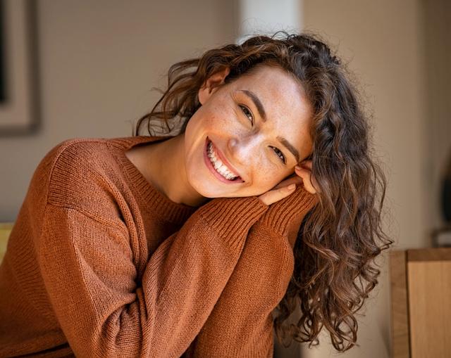 a woman in a brown sweater is smiling while sitting on a couch .