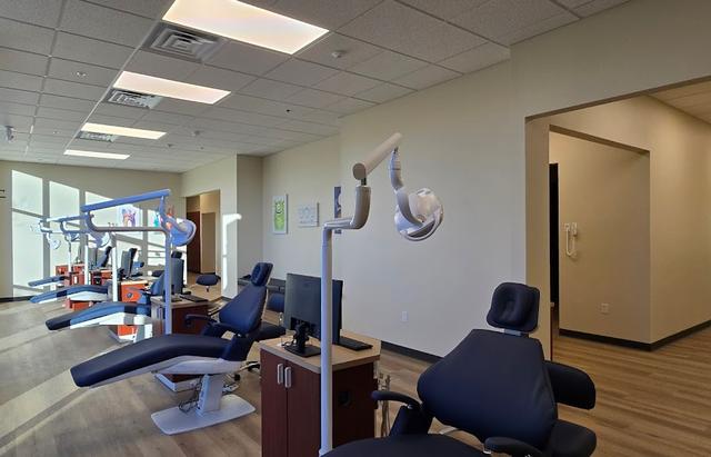 A spacious room in a dental office featuring several blue patient chairs, dental lights, and monitors.