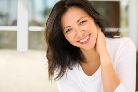 a woman in a white shirt is smiling with her hand on her neck .