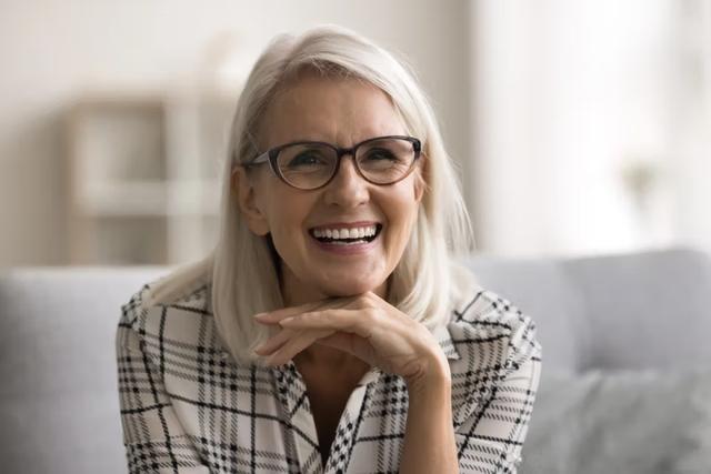 an older woman wearing glasses is smiling while sitting on a couch .
