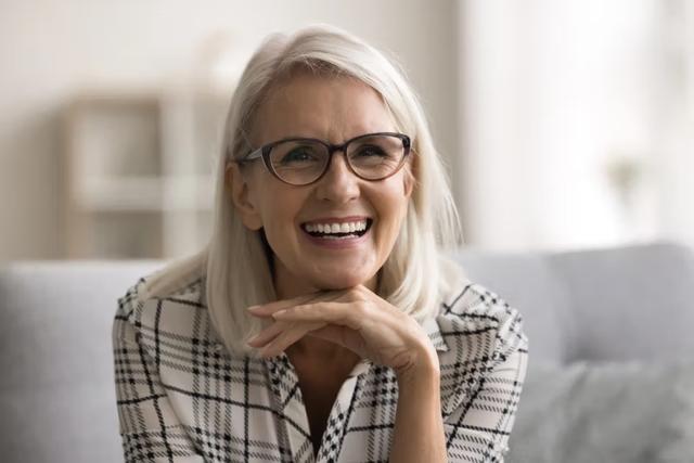 an older woman wearing glasses is smiling while sitting on a couch .