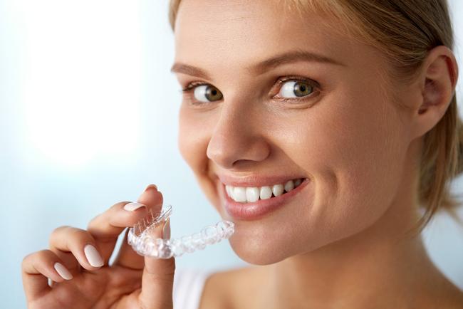 a woman is smiling while holding a clear brace on her finger .