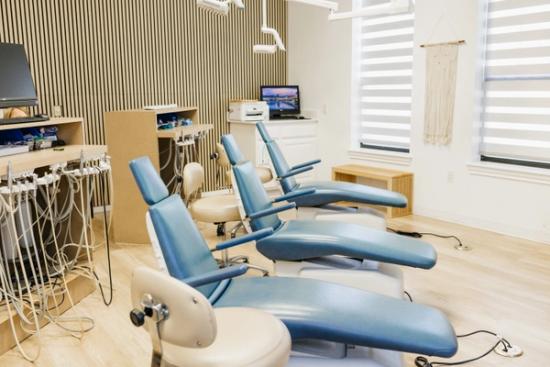 A modern dental office with three blue dental chairs, dental equipment, and light wood finishes.