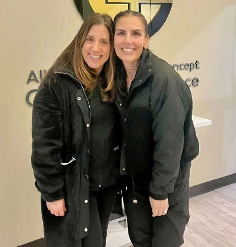two women are posing for a picture in front of a sign that says concept