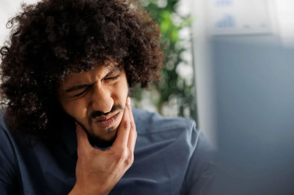 a man with curly hair is holding his mouth in pain