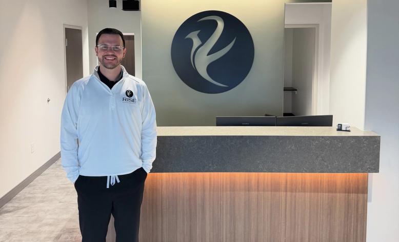 A modern reception area with an exposed black ceiling, a wood and stone reception desk, a logo on the back wall, and dark leather waiting chairs.
