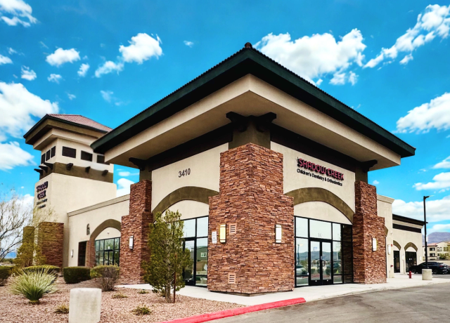 Exterior of Shadow Creek Children's Dentistry & Orthodontics, a modern building with stone accents and a tower, under a blue sky.