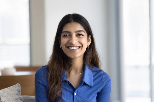 a woman in a blue shirt is smiling while sitting on a couch .