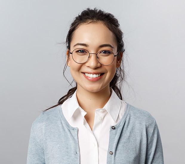 a woman wearing glasses and a blue cardigan is smiling .