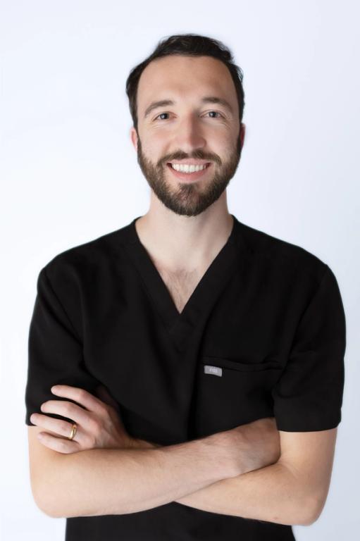 a man with a beard wearing a black scrub top has his arms crossed