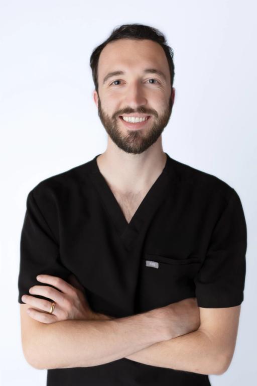 a man with a beard wearing a black scrub top has his arms crossed