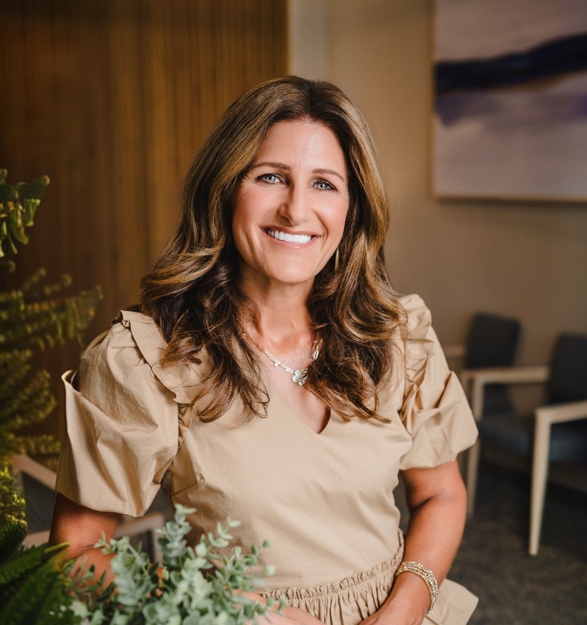a woman in a tan dress is smiling and holding a plant in a waiting room .