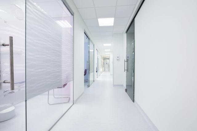 a long hallway in a hospital with glass doors and white walls .