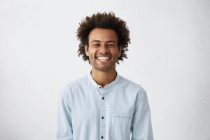 a young man with curly hair is smiling with his eyes closed .