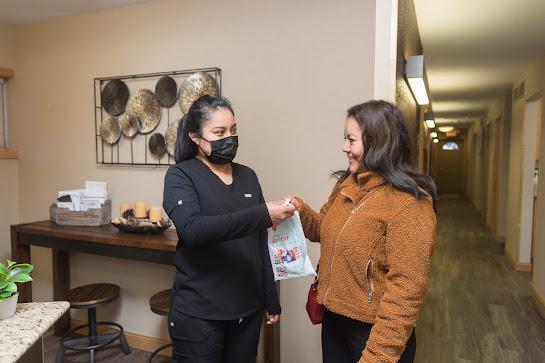 a woman wearing a mask is giving a bag to another woman in a hallway .