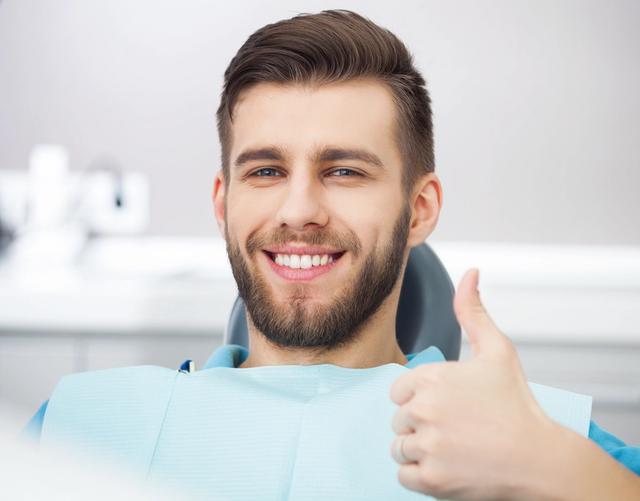 a man is sitting in a dental chair and smiling while giving a thumbs up .