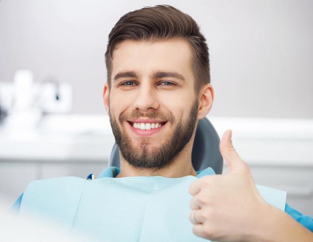 a man is sitting in a dental chair and smiling while giving a thumbs up .