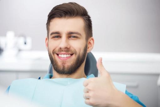 a man is sitting in a dental chair and smiling while giving a thumbs up .