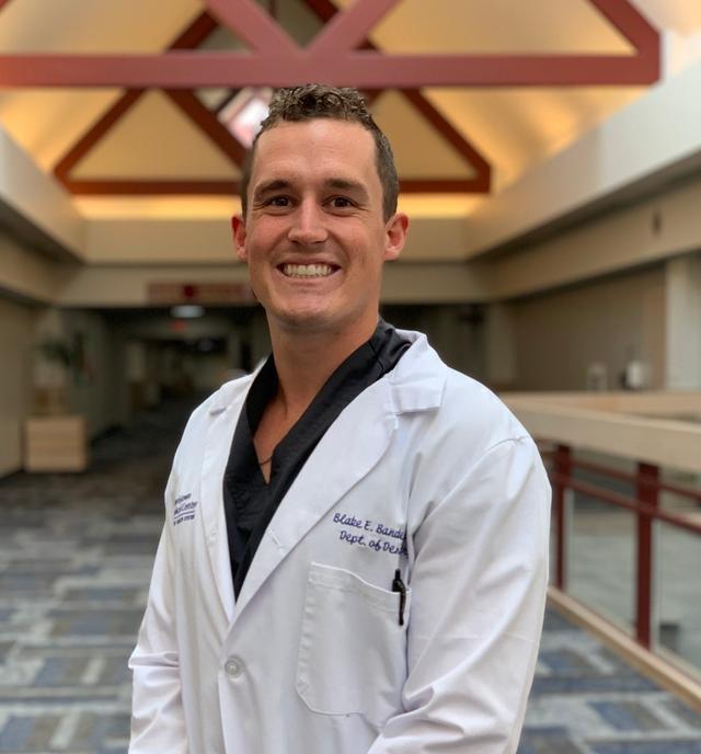 a man in a white lab coat is smiling in a hallway .