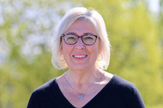 a woman wearing glasses and a necklace is smiling for the camera .