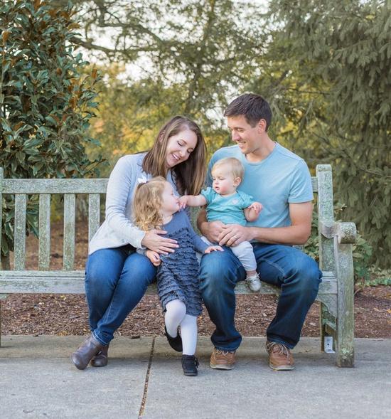 a family is sitting on a bench in a park .