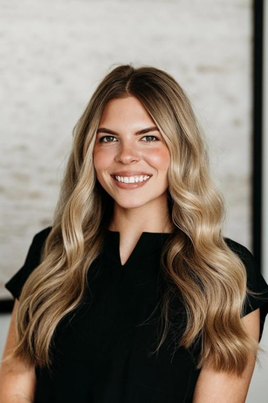 A smiling woman with long, wavy blonde hair and a black top.