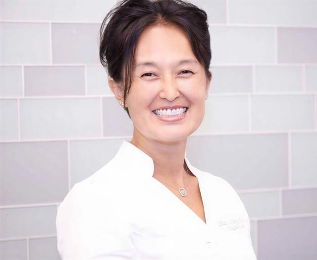 Smiling woman in a white uniform against a tiled wall.