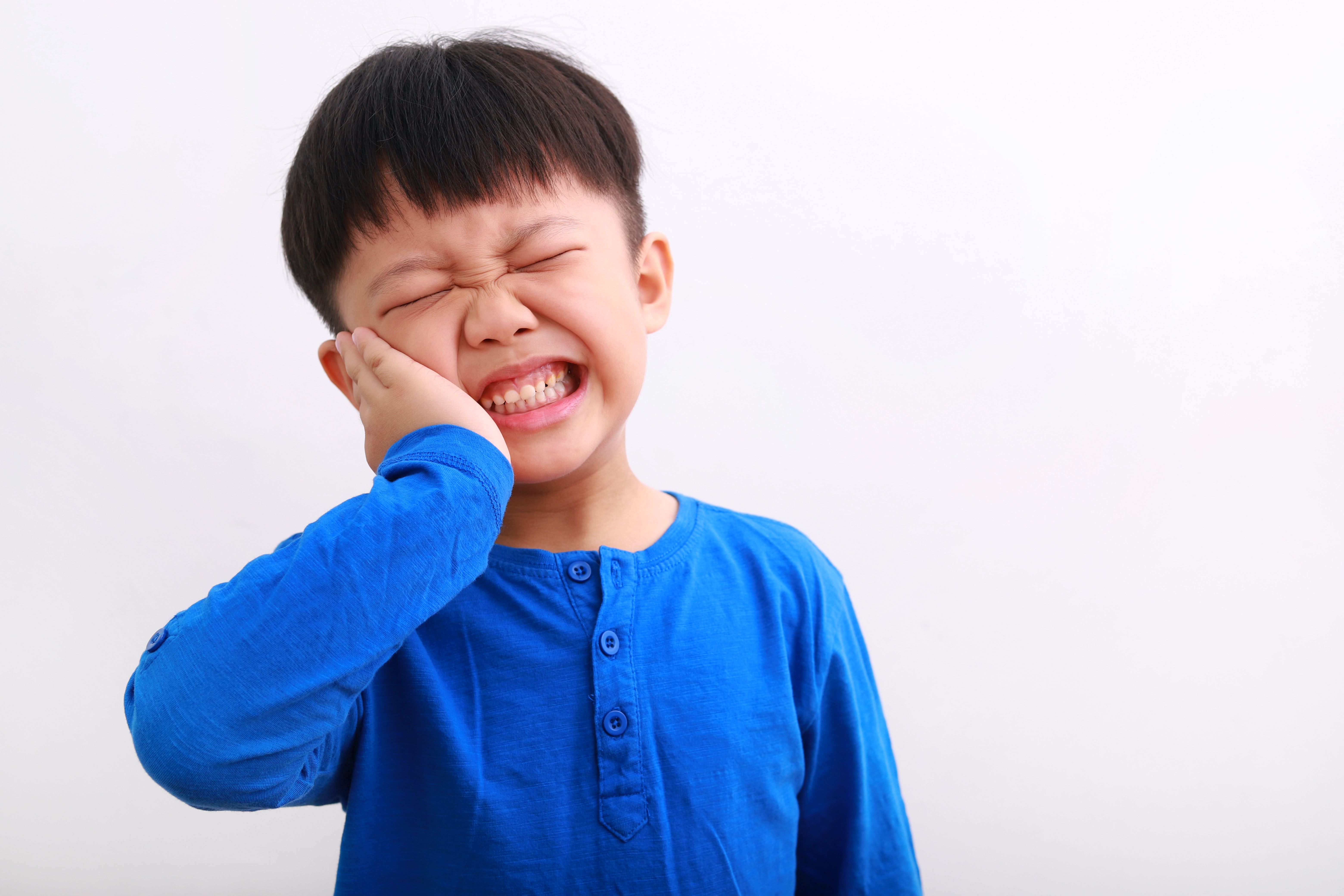 a young boy is holding his face in pain because he has a toothache .