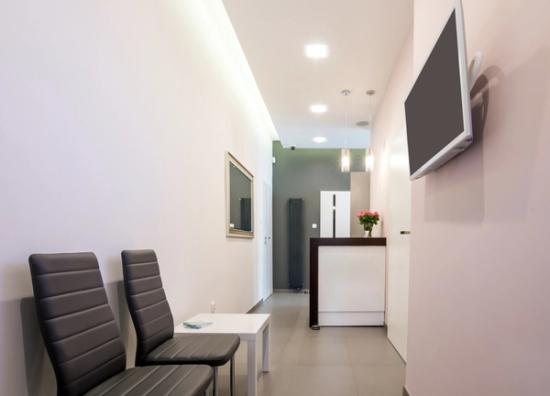 a waiting room with chairs , a table and a flat screen tv on the wall .