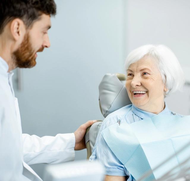 an elderly woman is smiling while sitting in a dental chair .