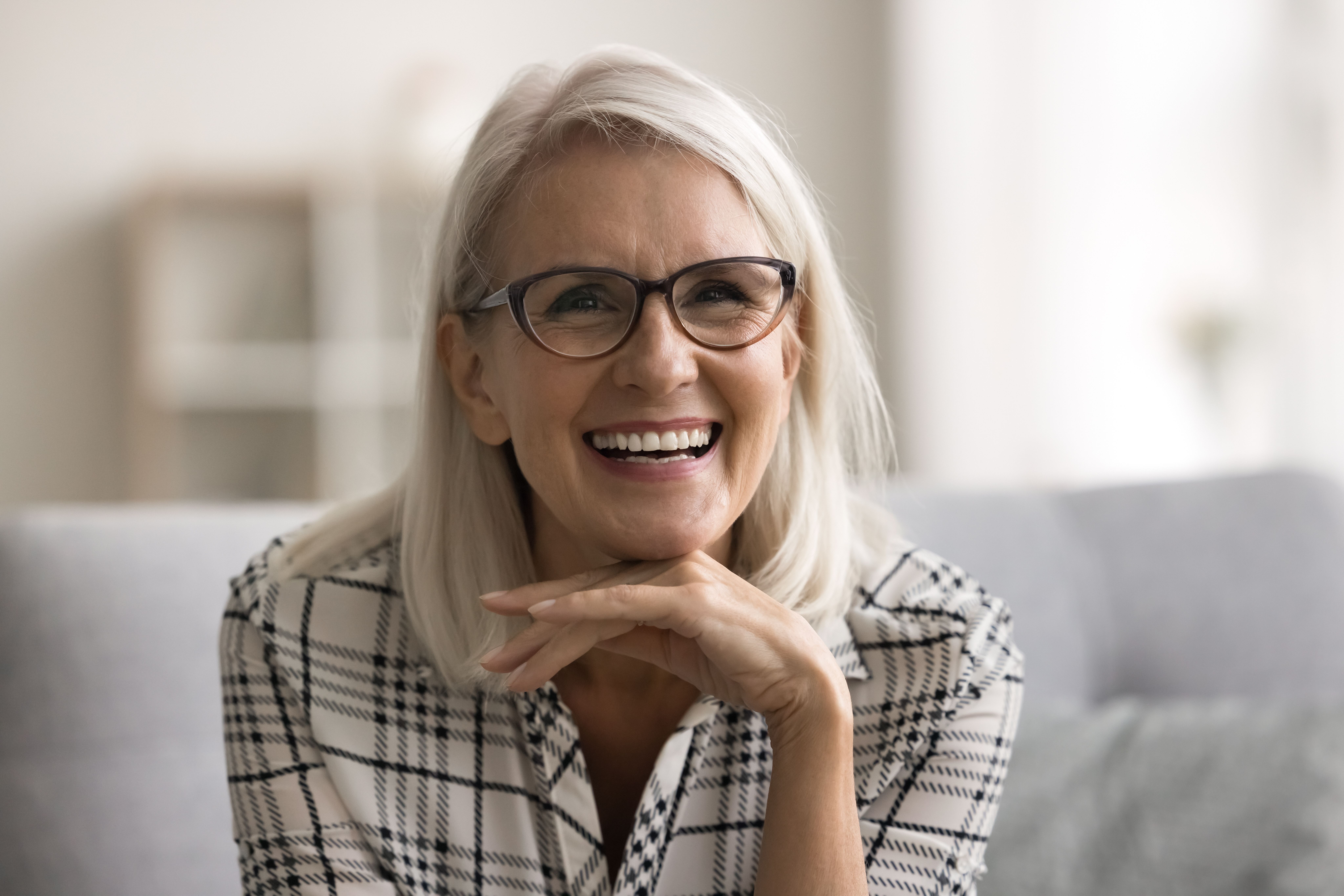 an older woman wearing glasses is smiling while sitting on a couch .