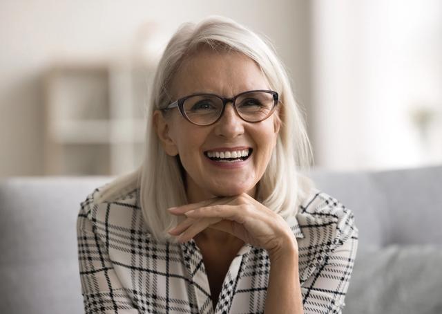 an older woman wearing glasses is smiling while sitting on a couch .