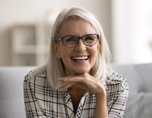 an older woman wearing glasses is smiling while sitting on a couch .