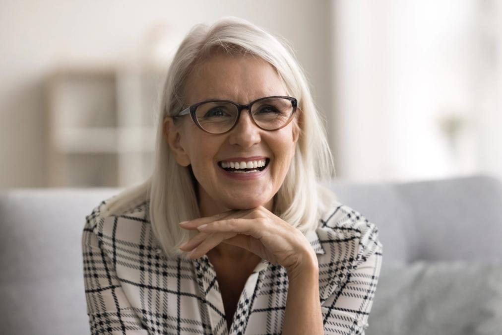 an older woman wearing glasses is smiling while sitting on a couch .