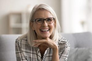 an older woman wearing glasses is smiling while sitting on a couch .