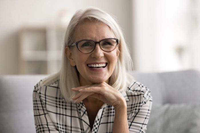 an older woman wearing glasses is smiling while sitting on a couch .