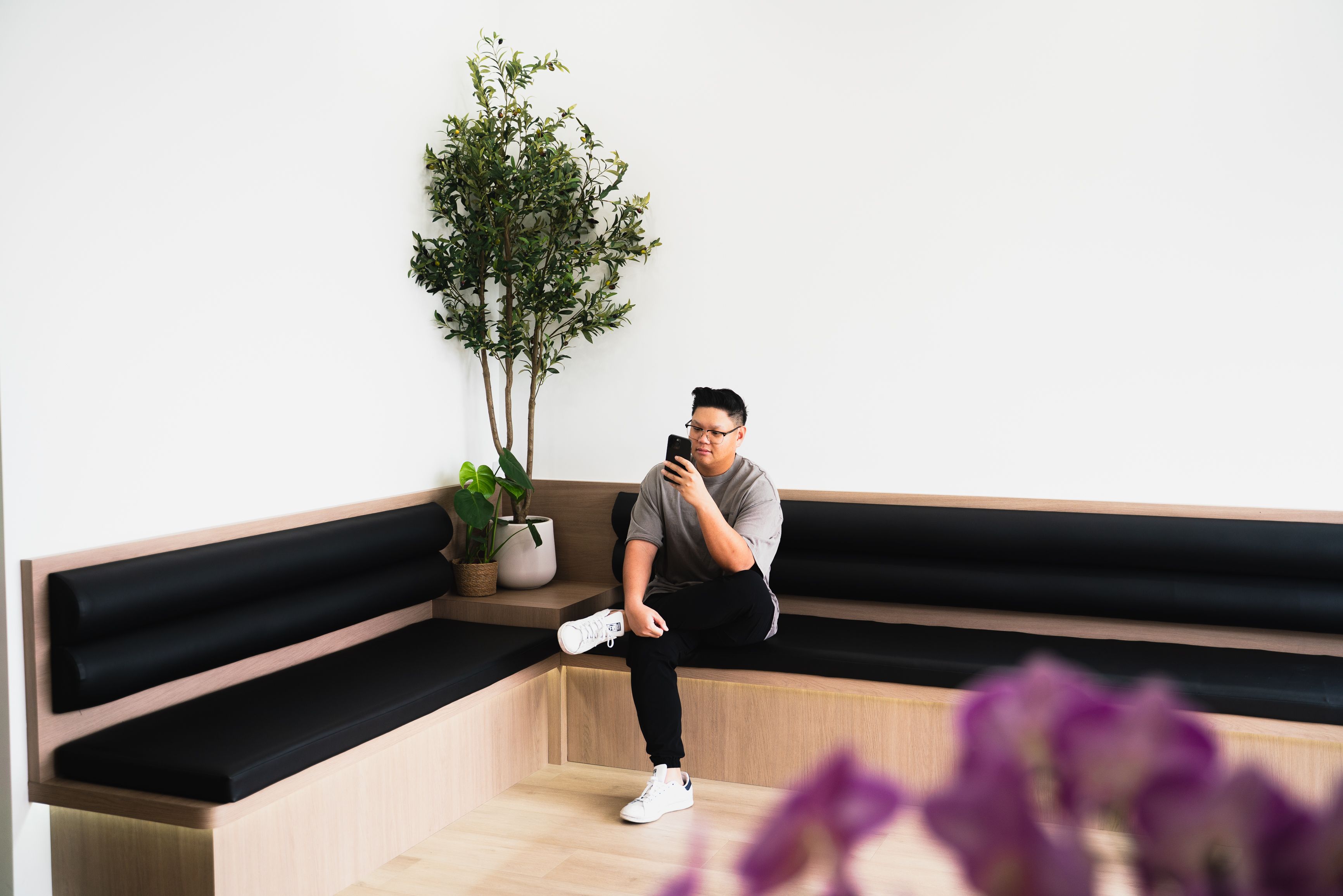 A person sits on a modern corner bench, looking at their phone.