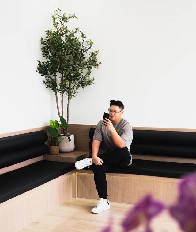 A person sits on a modern corner bench, looking at their phone.