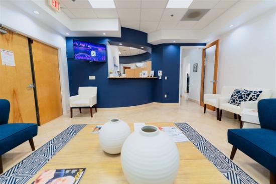 a waiting room at a dental office with chairs , a table and vases .