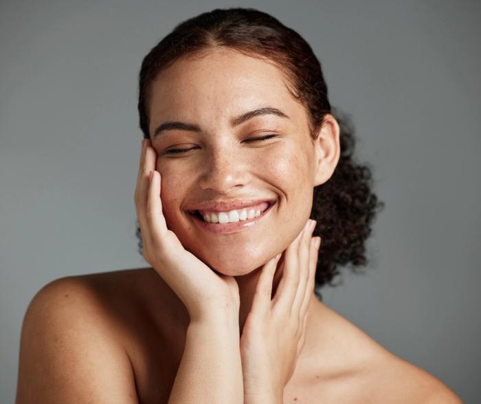 a woman is smiling and touching her face with her hands .