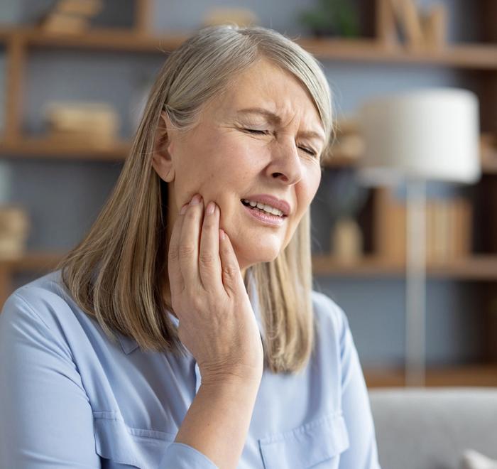 an elderly woman is holding her face in pain because of a toothache .