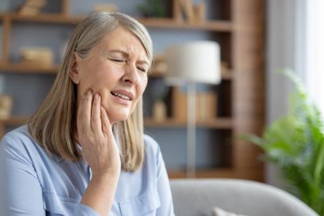 an elderly woman is holding her face in pain because of a toothache .