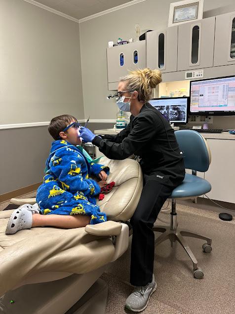 a young boy is sitting in a dental chair while a dentist examines his teeth .