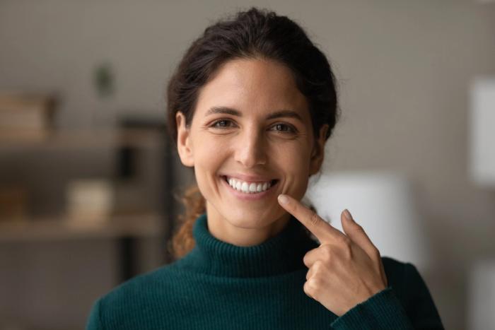 a woman is pointing at her smile with her finger .