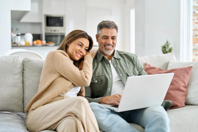 a man and a woman are sitting on a couch using a laptop computer .
