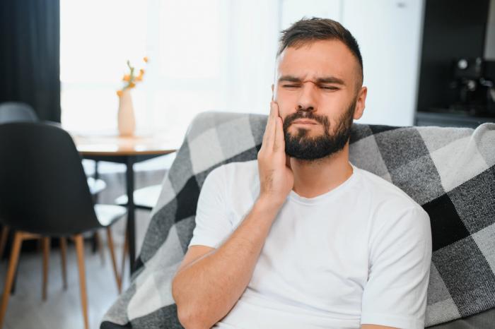 a man with a beard is sitting on a couch with a toothache .