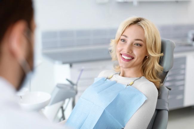 Smiling blonde woman in a dental chair looking at a dentist.