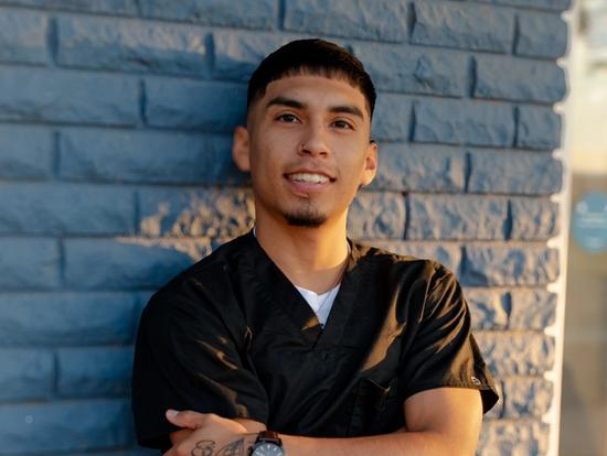 a young man in a black scrub is standing in front of a blue brick wall with his arms crossed .