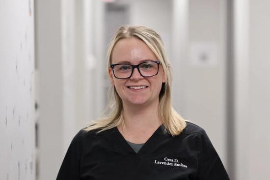 a woman wearing glasses and a black scrub top is smiling for the camera .