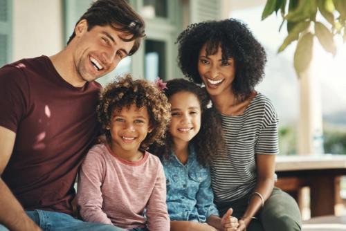 a family is sitting on a porch and smiling for the camera .